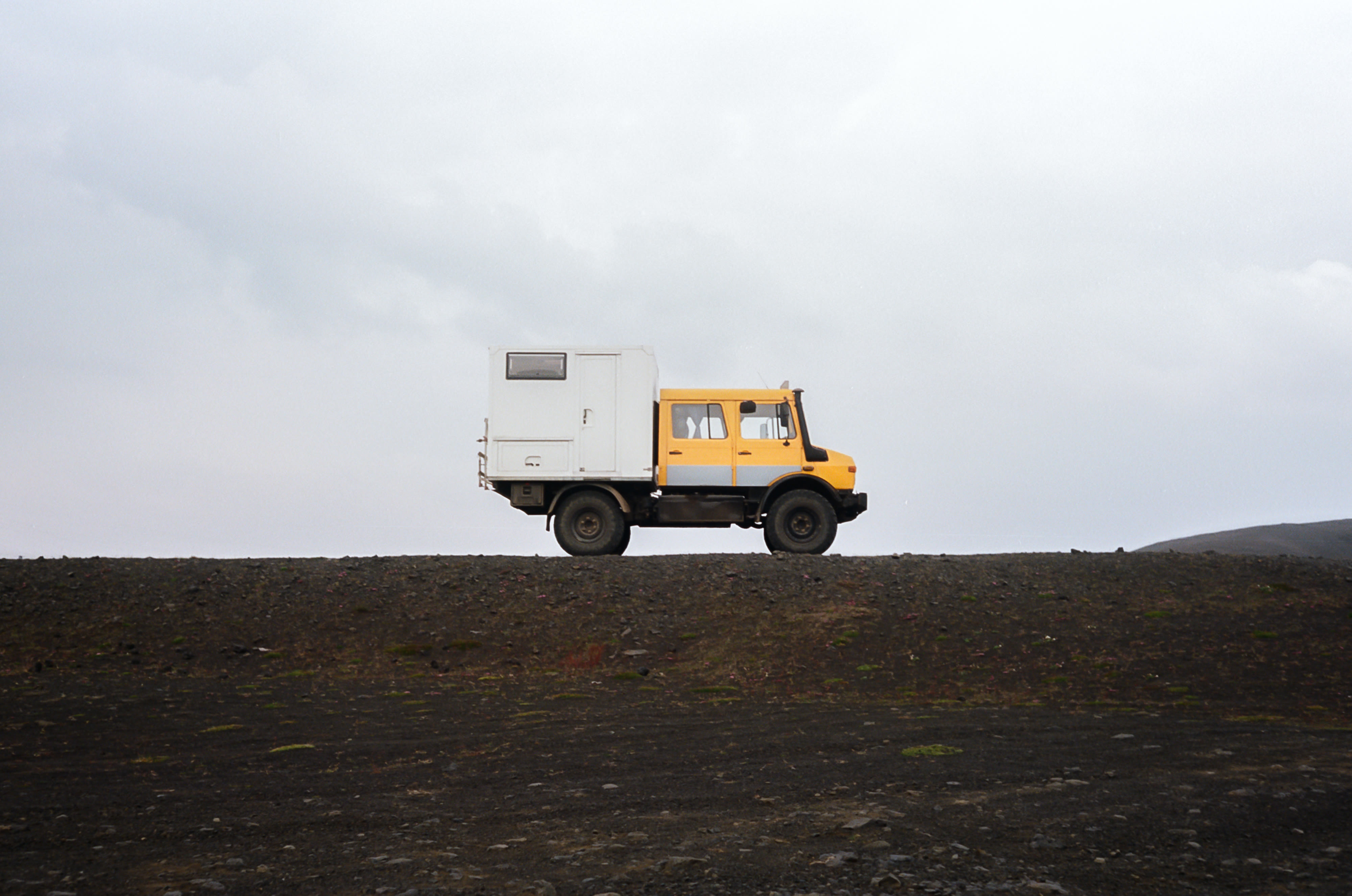 A yellow Unimog expedition truck parked on a gravel ridge near Sig&ouml;ldufoss, Iceland